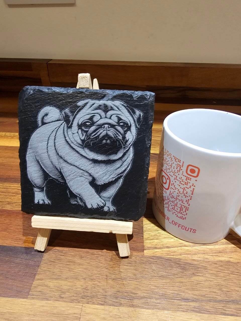 Pug edition Premium Custom Laser-Engraved Slate Coaster 10cm displayed on an easel next to a white mug.