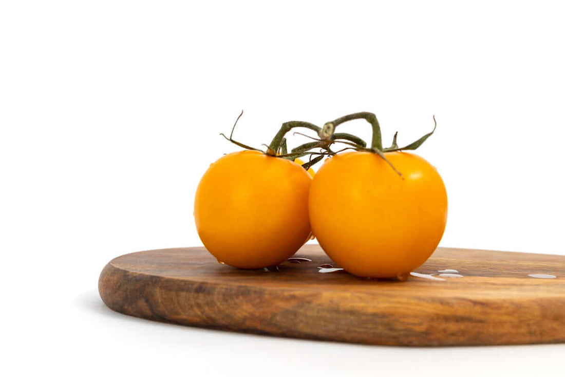 two yellow tomatoes sitting on top of a wooden cutting board