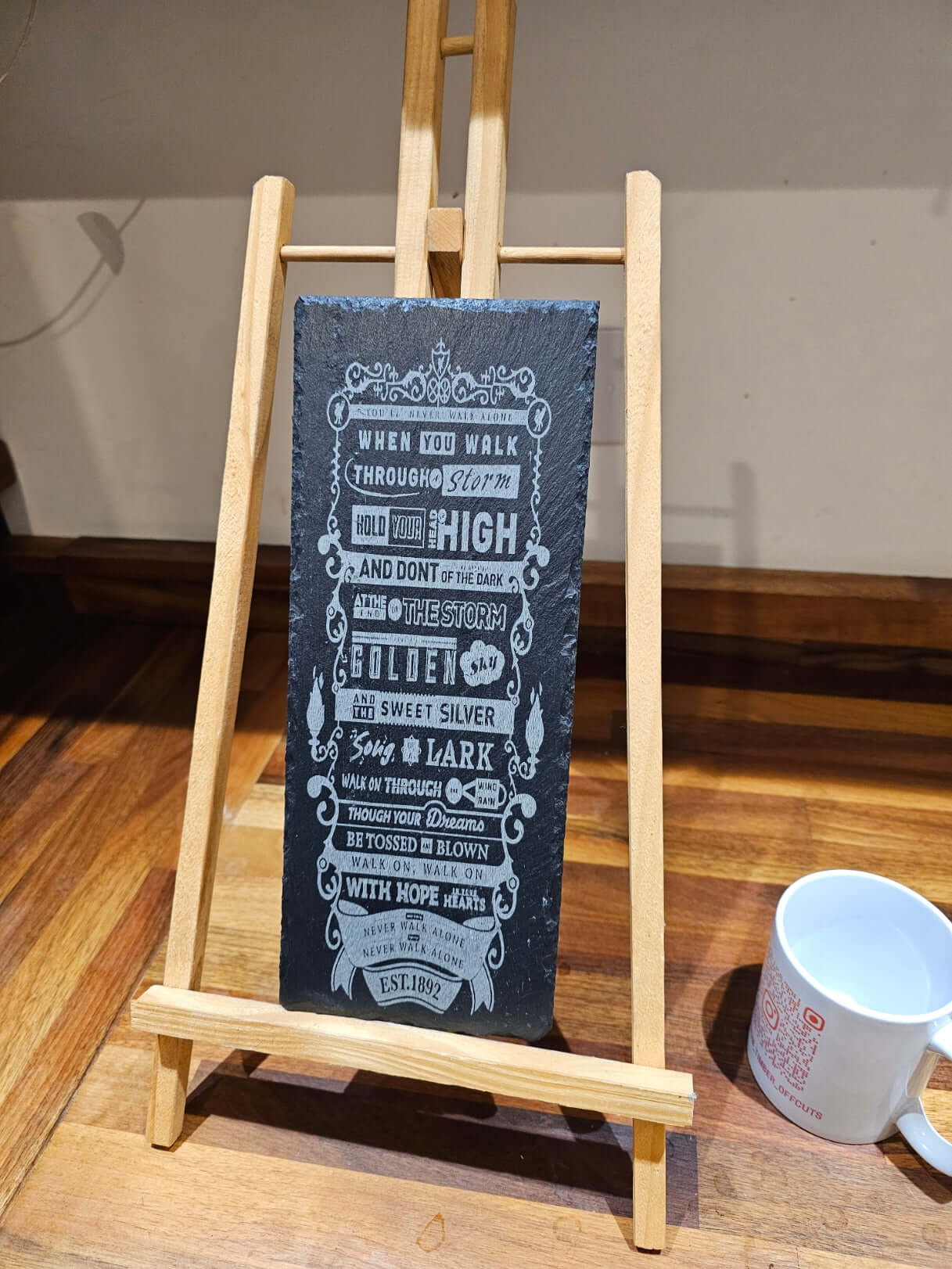 engraved slate plaque you'll never walk alone displayed on an easel next to a white mug.