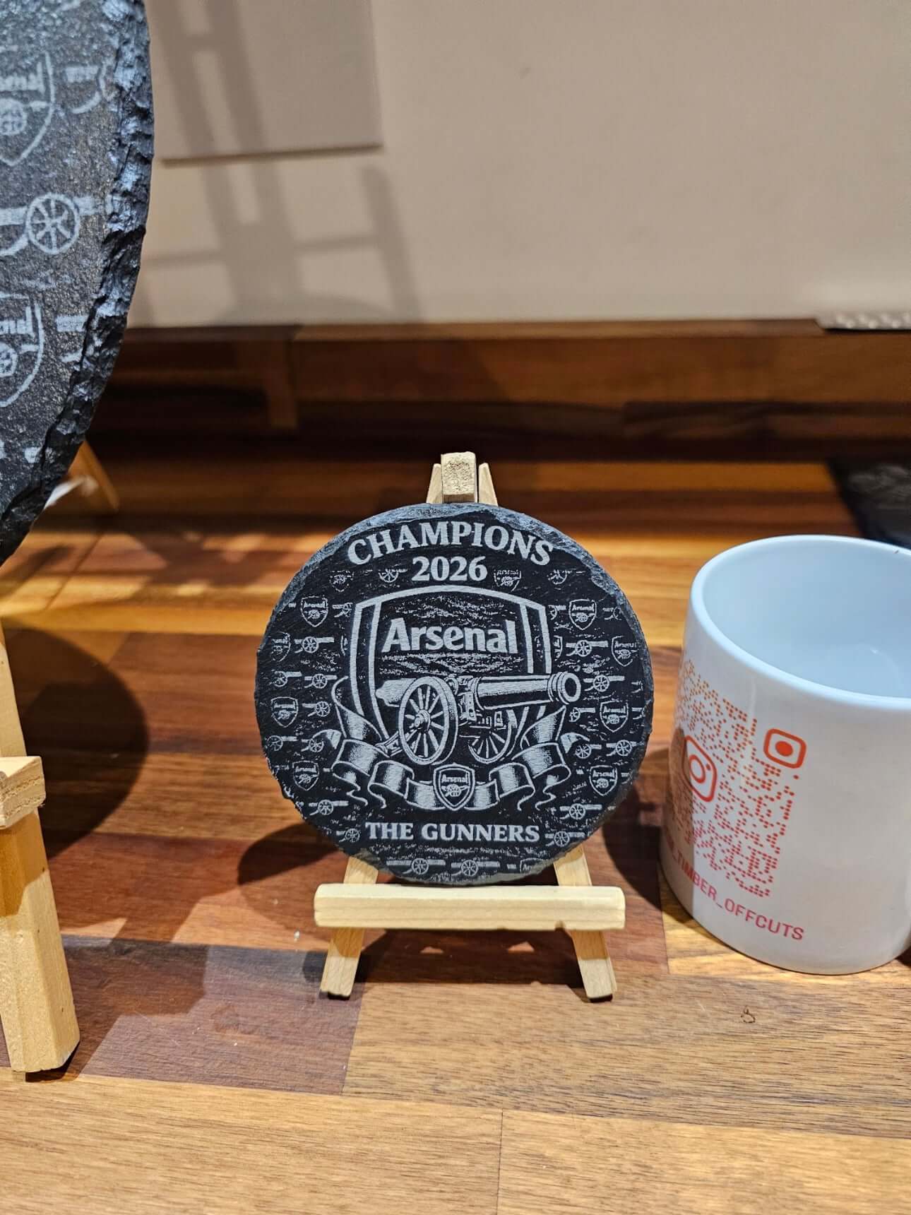 Arsenal Champions 2026 Engraved Slate Coaster displayed on a wooden stand, showcasing rich details.