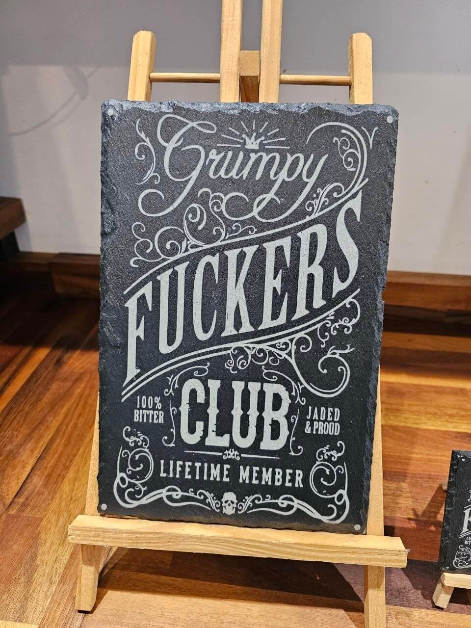 Slate plaque featuring the Grumpy Fuckers Club design, showcasing bold typography and decorative flourishes.